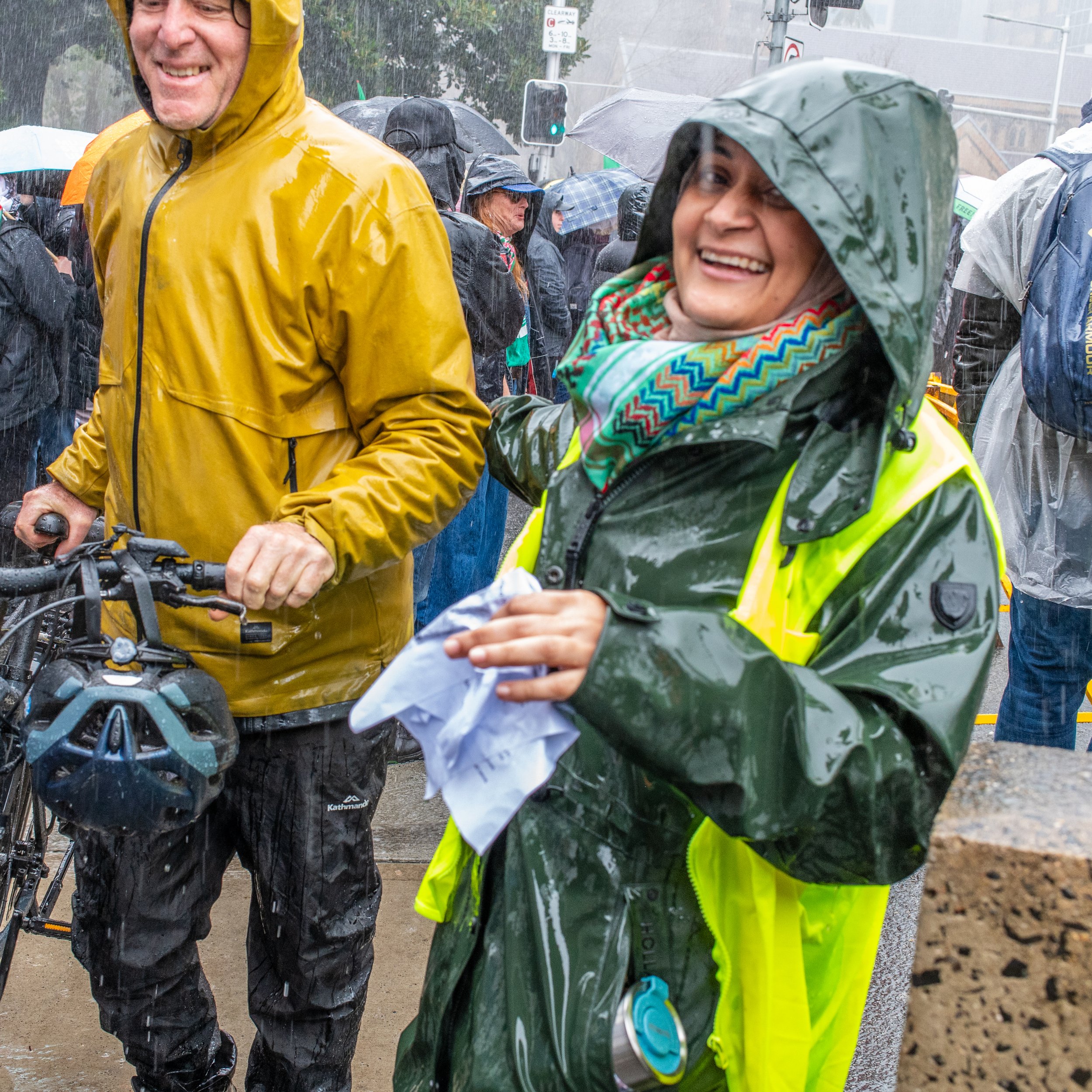 People in rain gear smiling and gathered in a crowd during a rainy outdoor event.