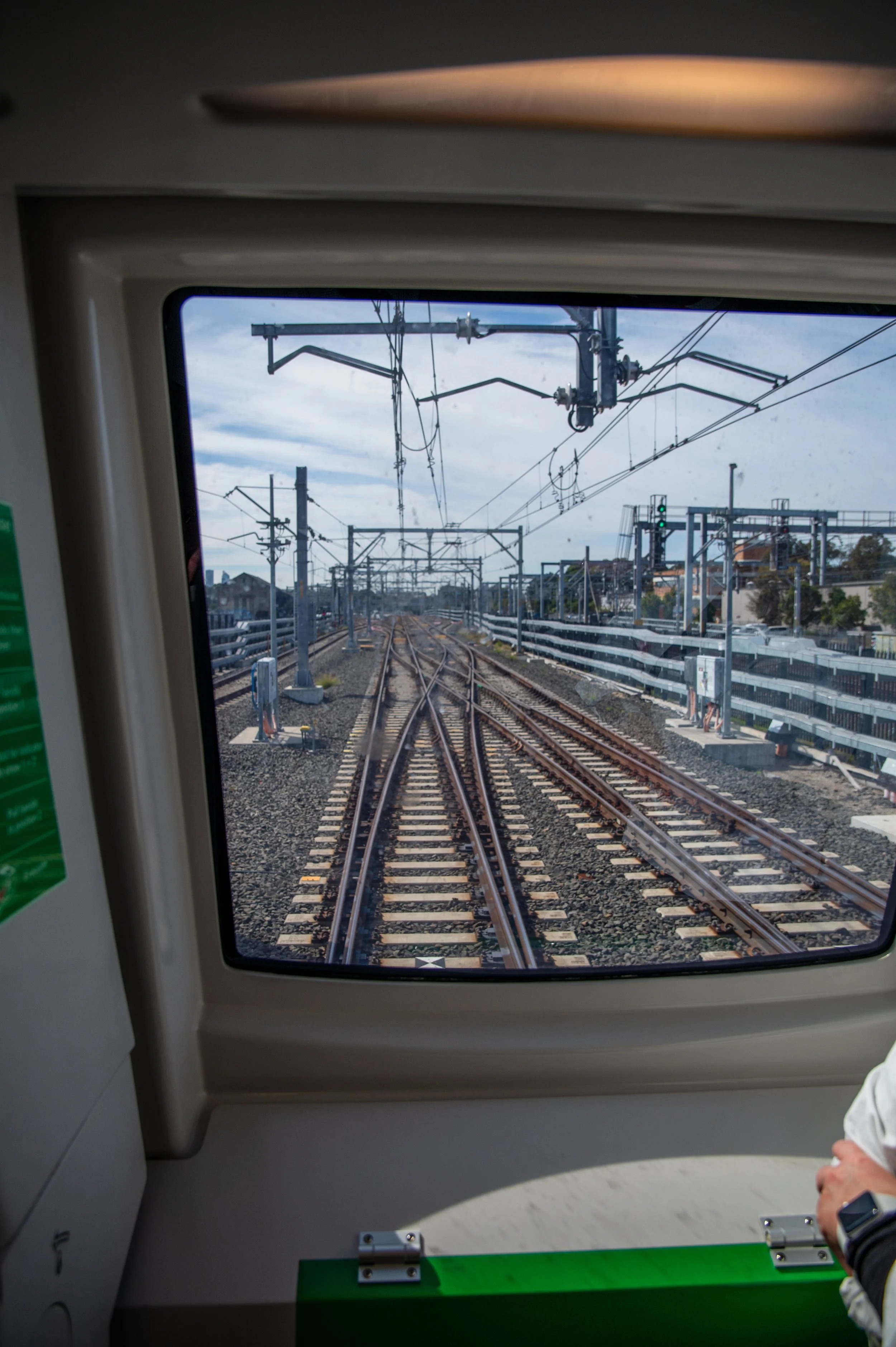 View from inside a train looking out the window at multiple railroad tracks and overhead electrical wires.