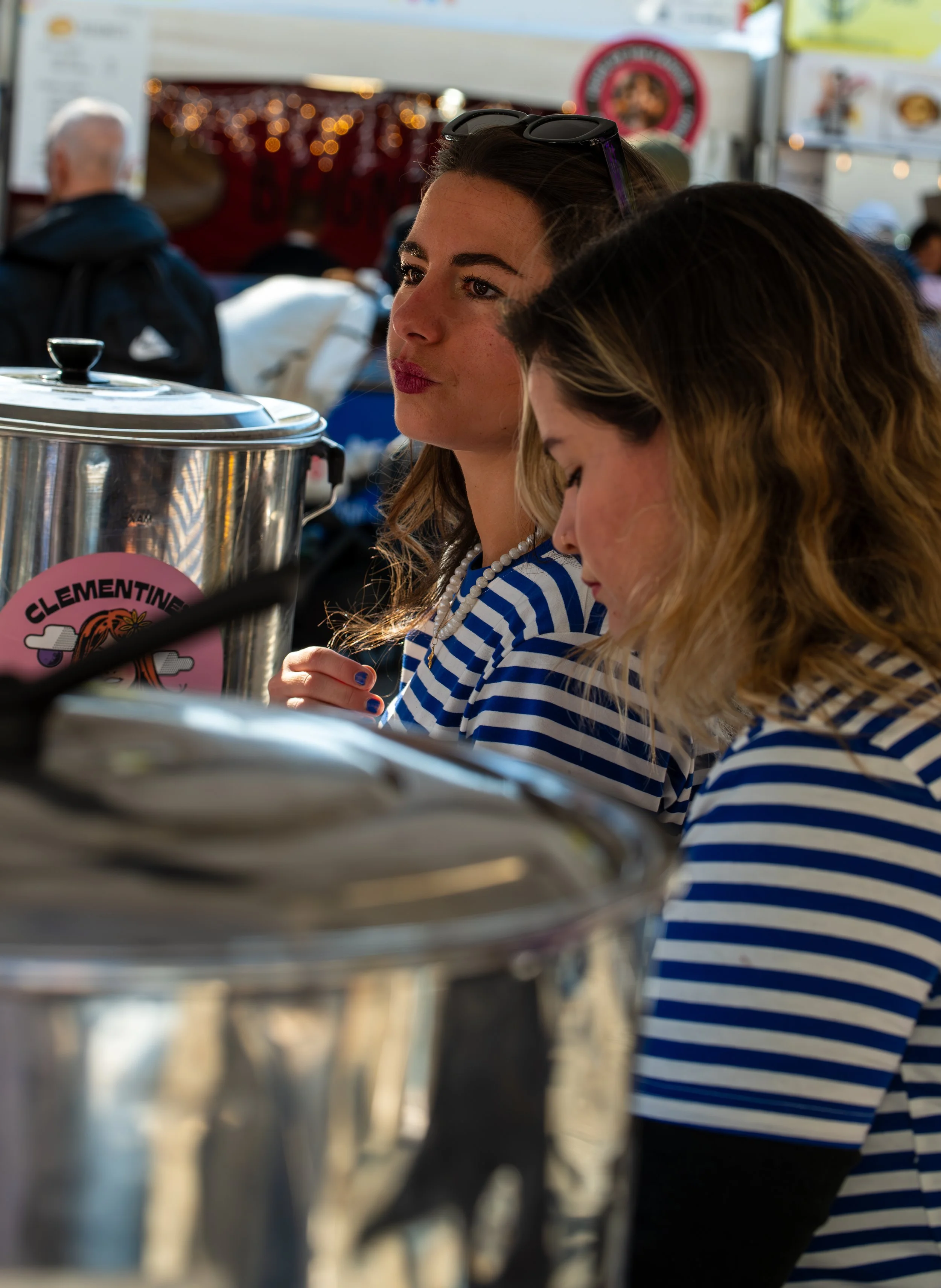 Two women in striped shirts sitting at a table with a large stainless steel container labeled "Clementine."
