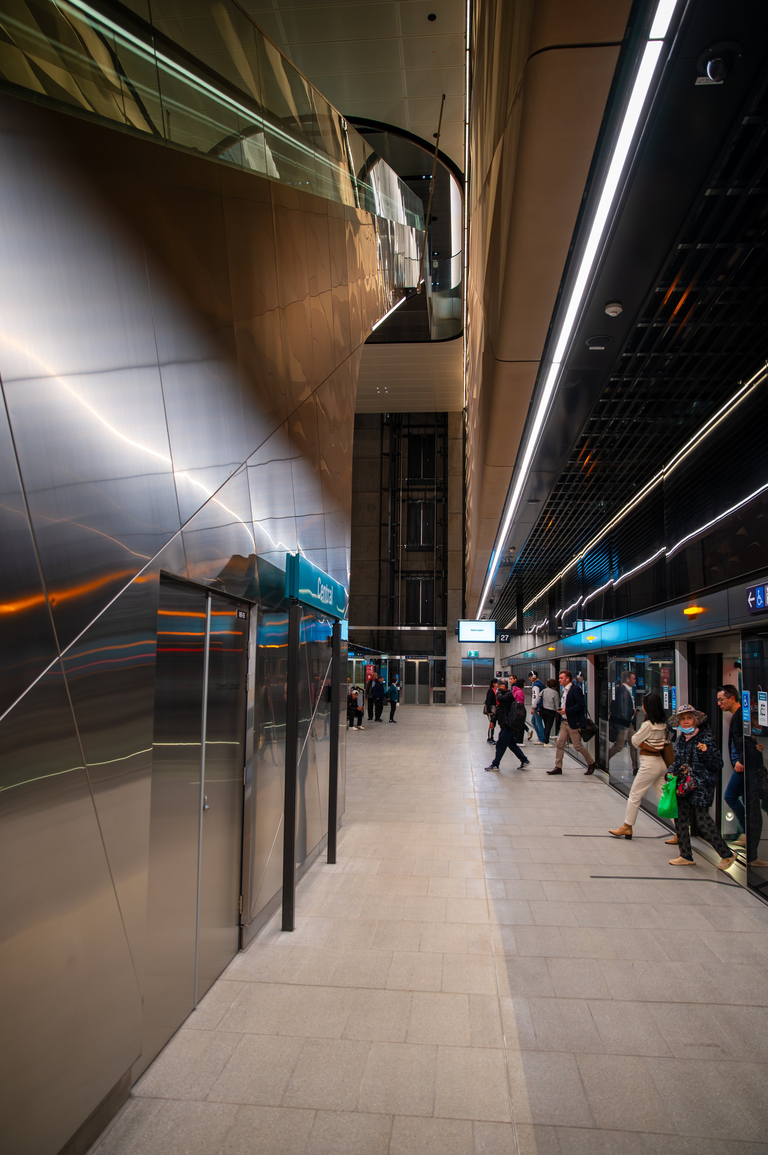 Interior of a modern airport terminal with people walking and waiting near the train or subway station entrance.