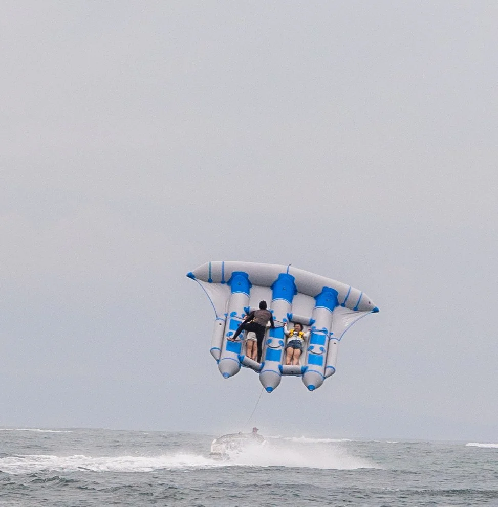 People parasailing over water with a boat below on a cloudy day.