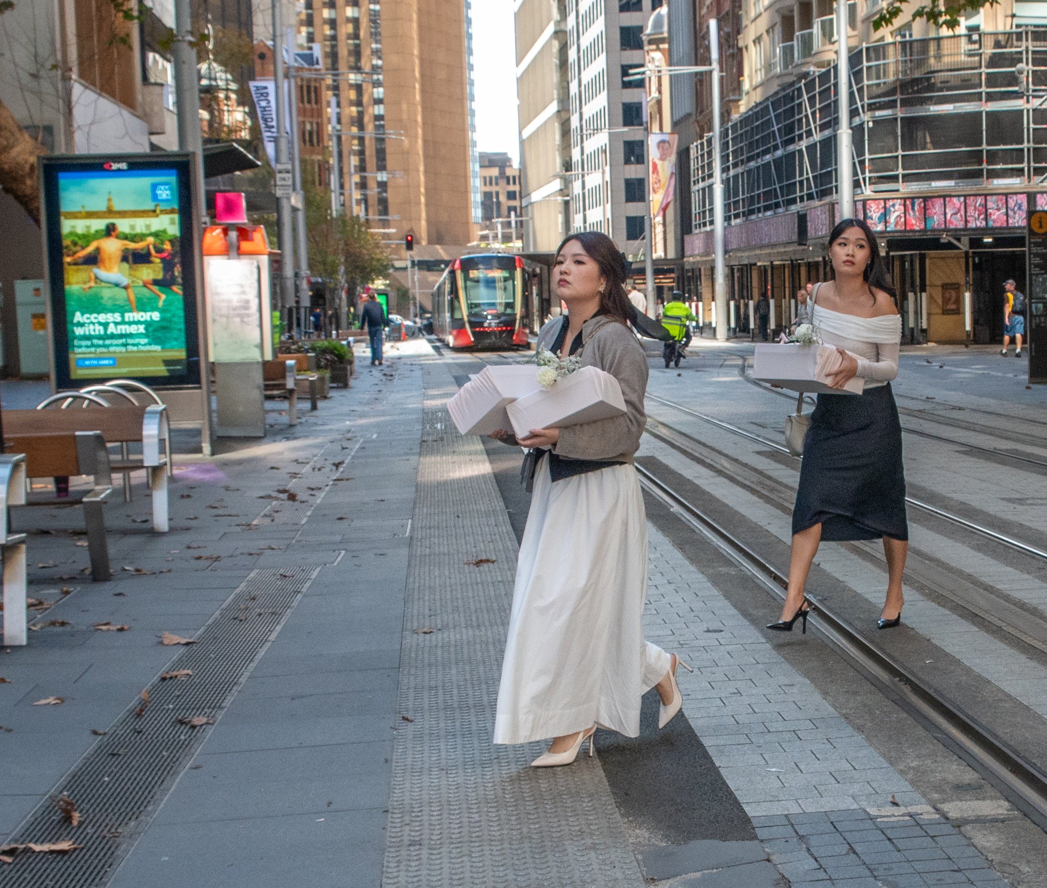 Two women walking on a city street, each carrying white boxes decorated with flowers.