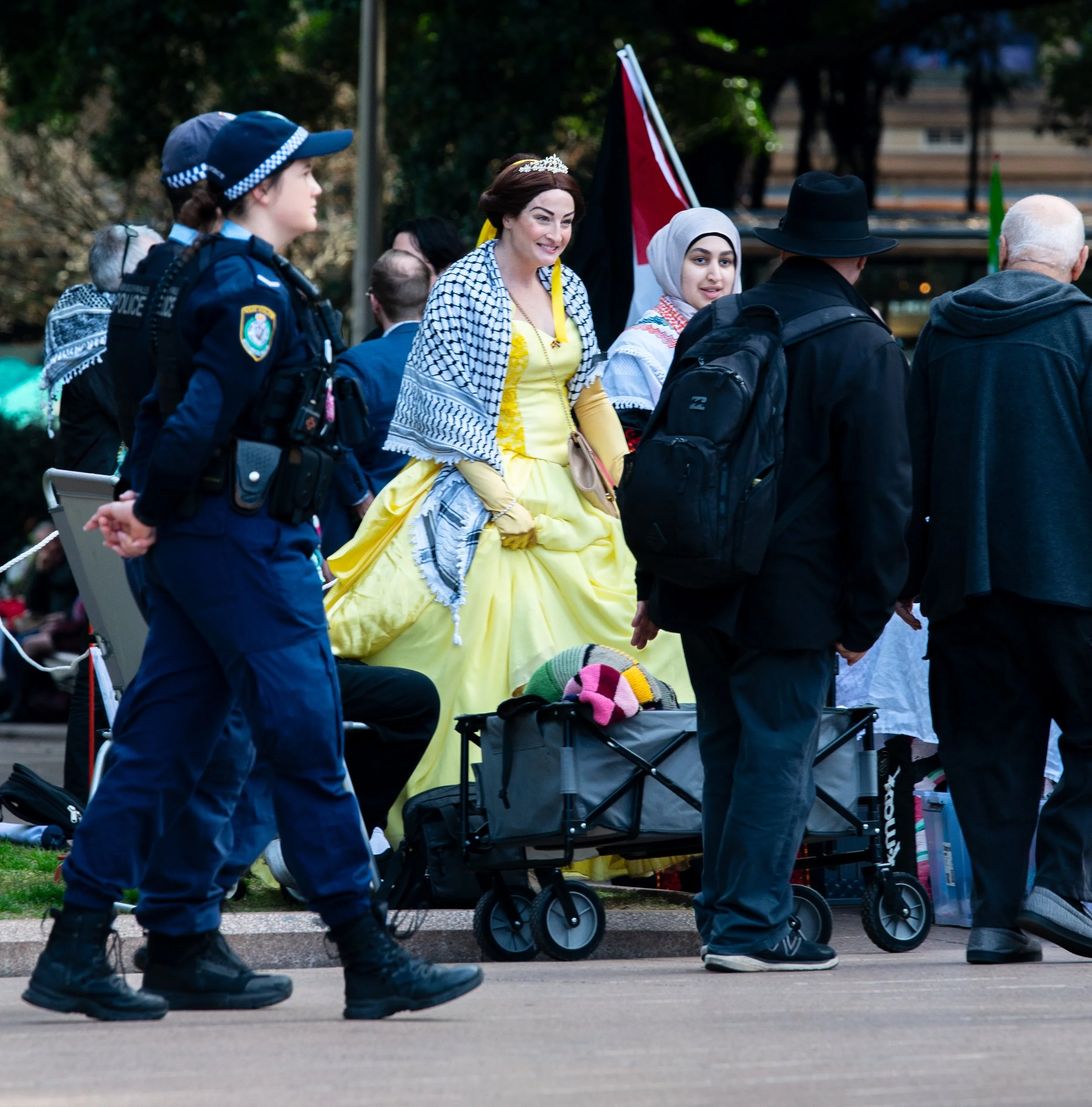 Women dressed in traditional Palestinian attire, with police officers and other people standing nearby in a park-like setting.