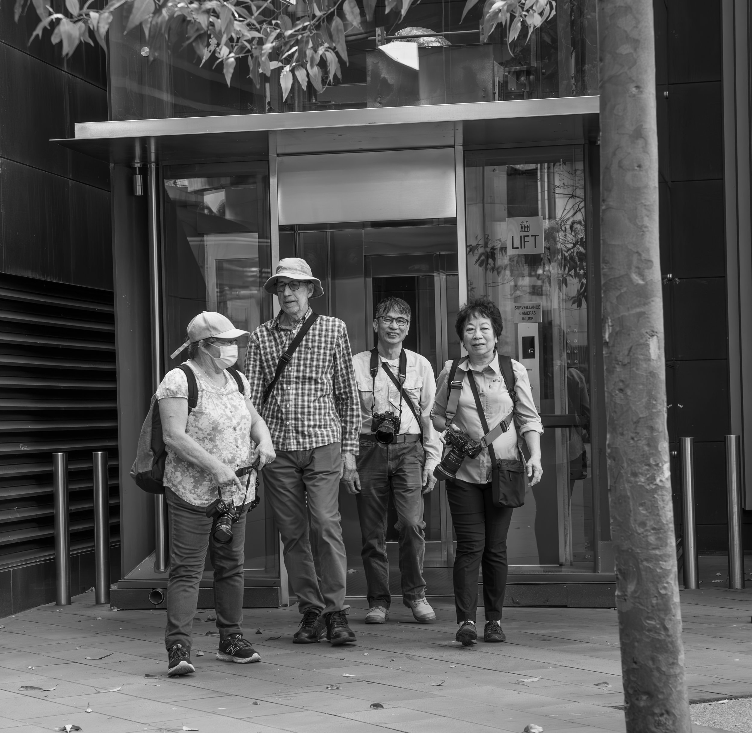 Four tourists with cameras exiting a building with an elevator, approaching the street.