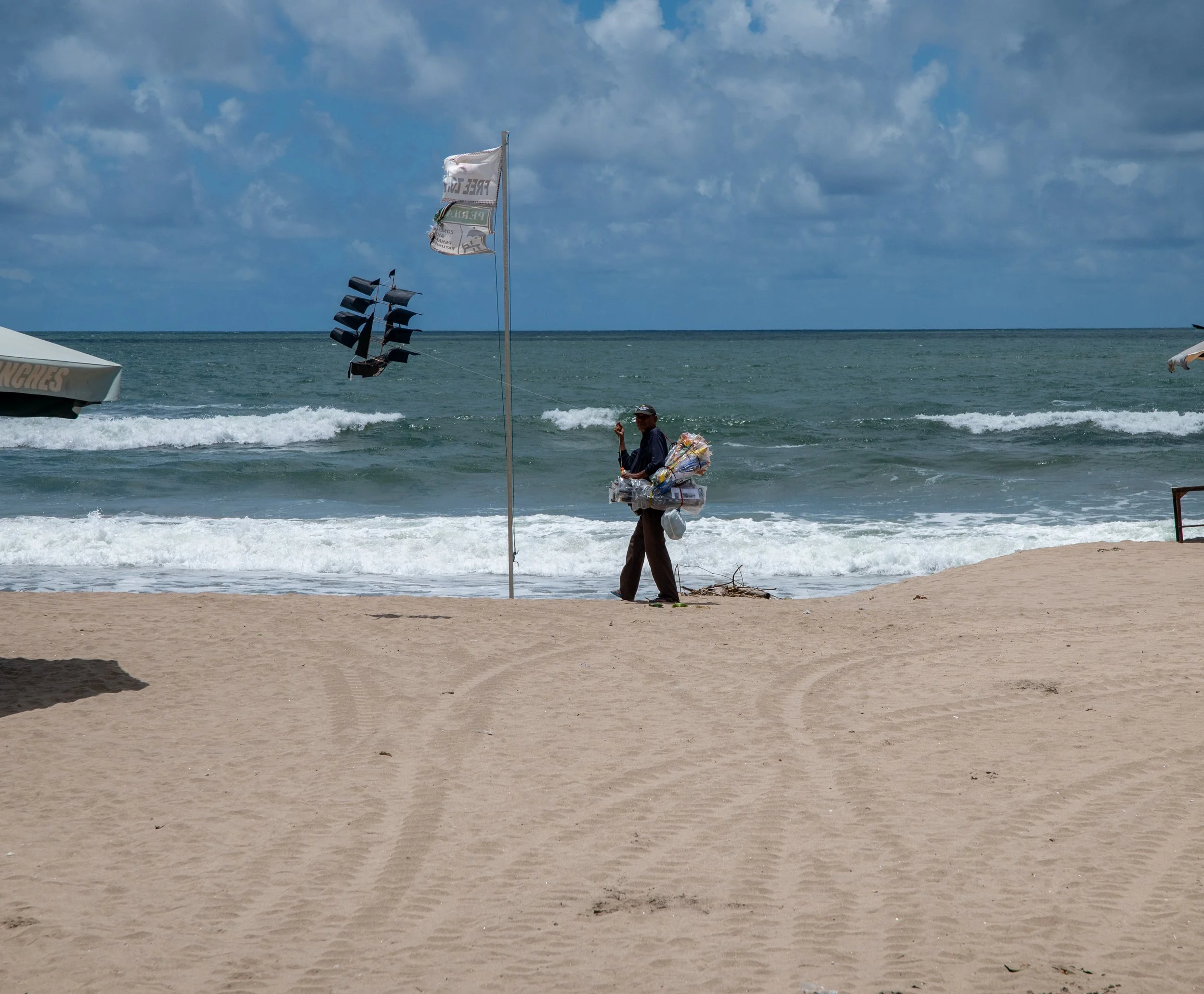 A person on the beach with a kite, beach umbrella, and the ocean in the background.