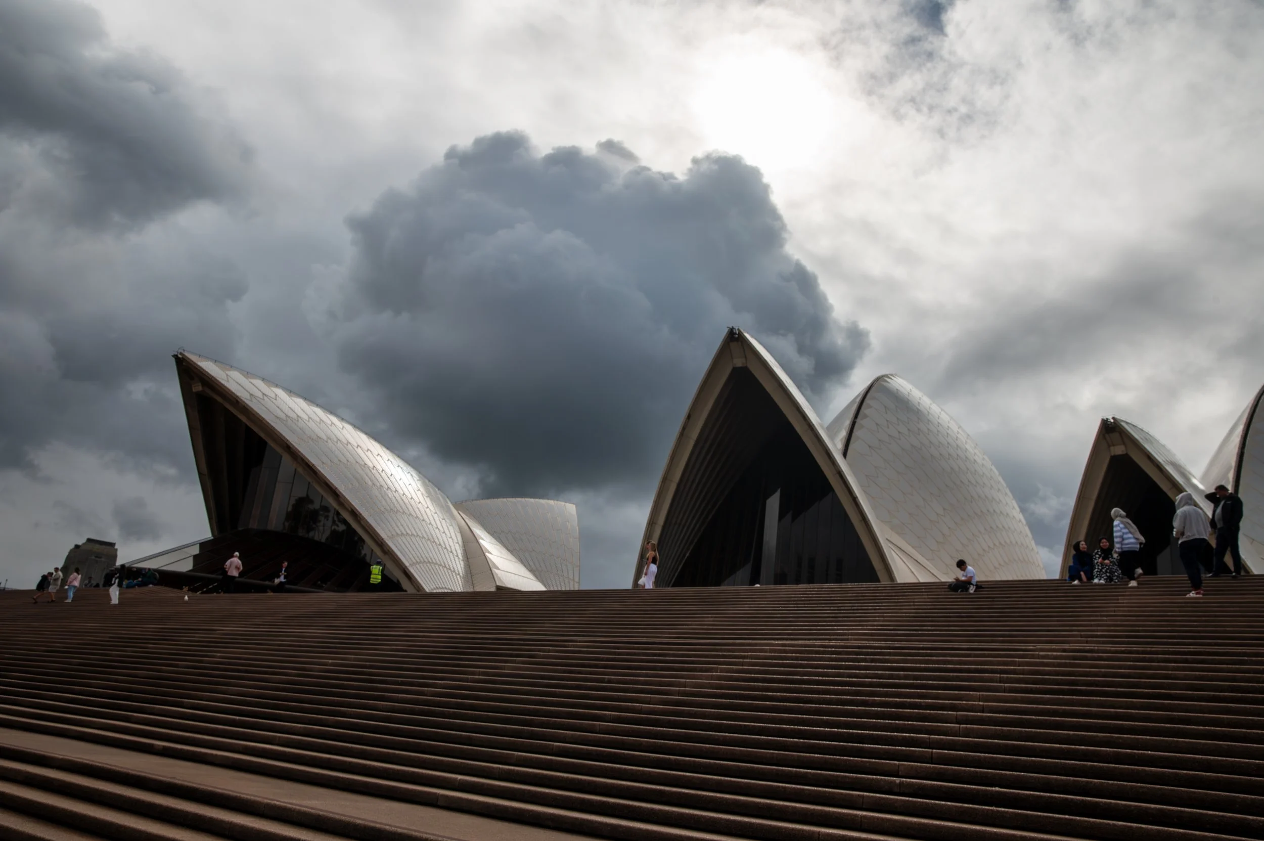 Sydney Opera House under dark, cloudy sky with people walking on steps