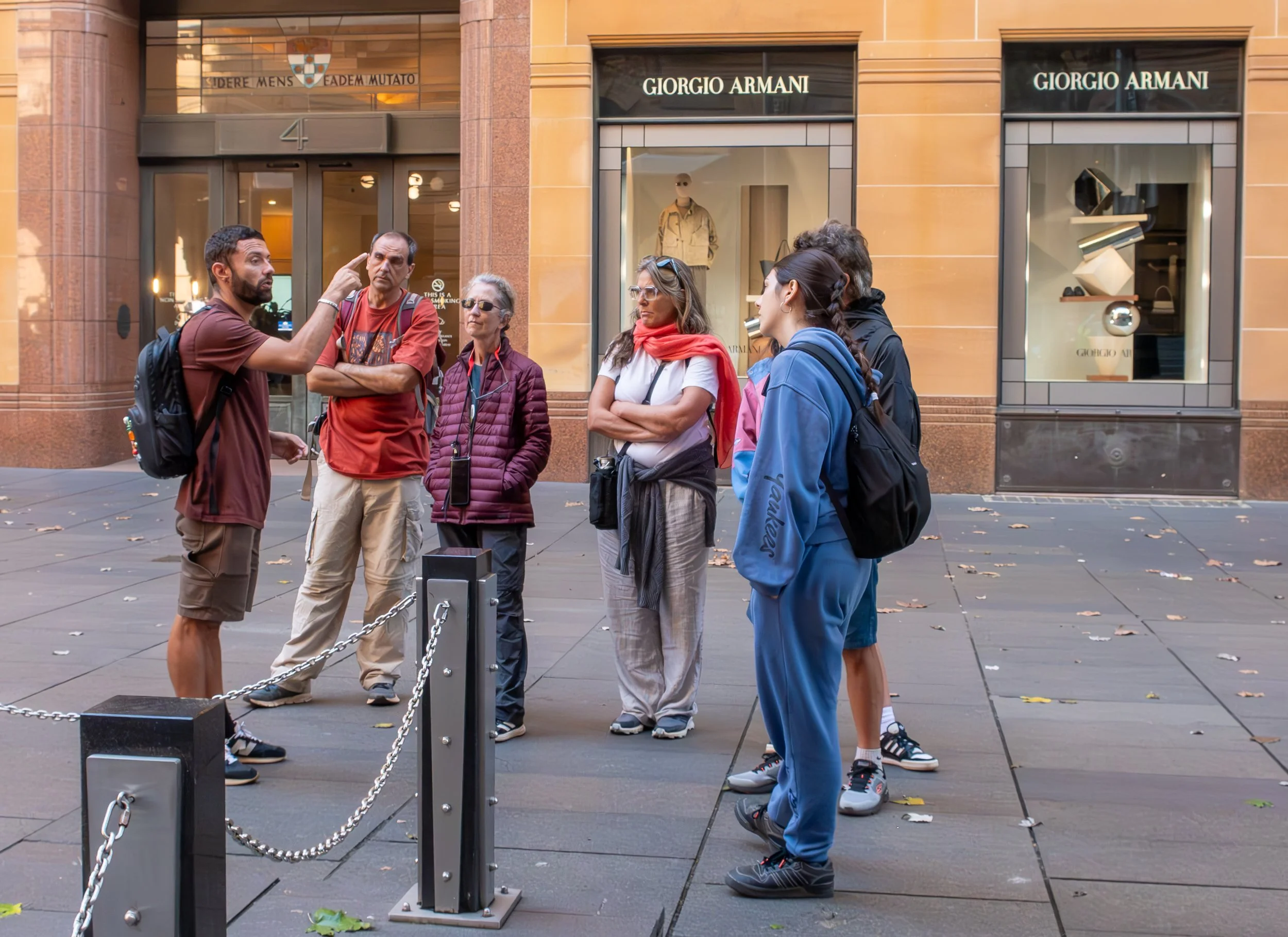 A tour guide leading a group of people on a city street, with Giorgio Armani storefronts in the background.