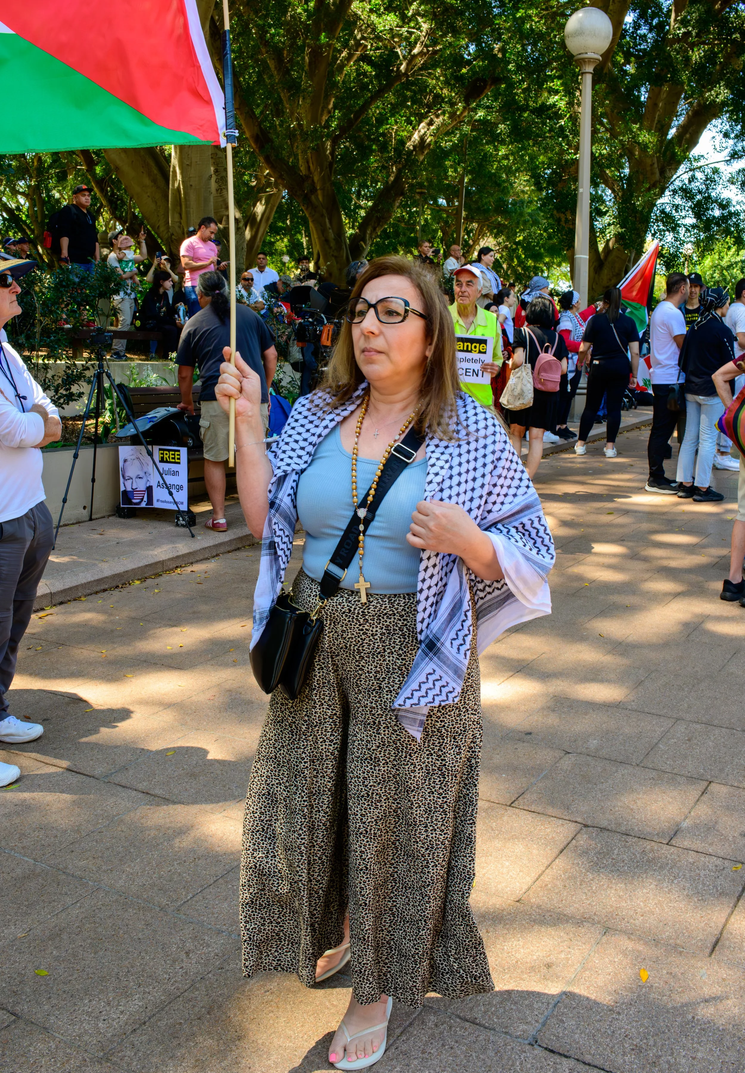 A woman holding a Palestinian flag at a protest or rally, surrounded by a crowd of people.