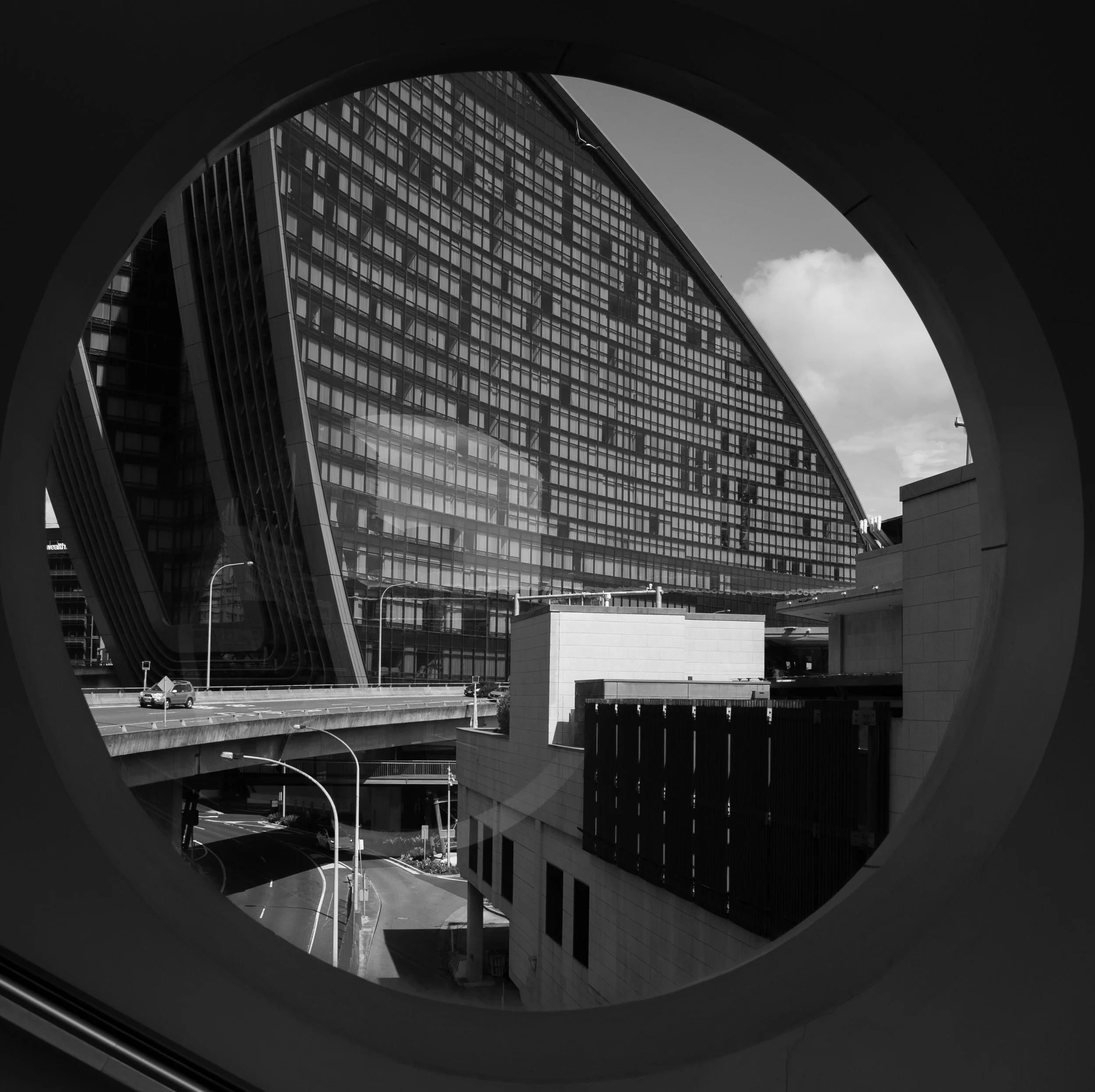View of a modern skyscraper with a curved glass facade through a circular window, black and white photograph.
