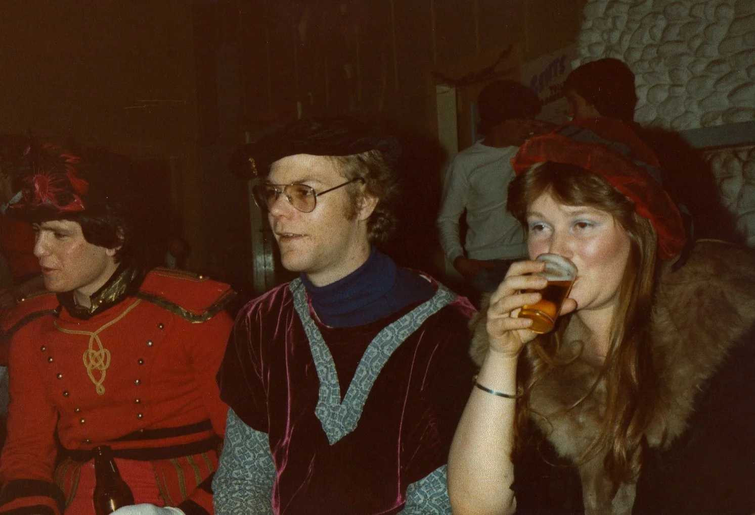 People dressed in medieval costumes sitting at a table, with at least one person drinking a beer.