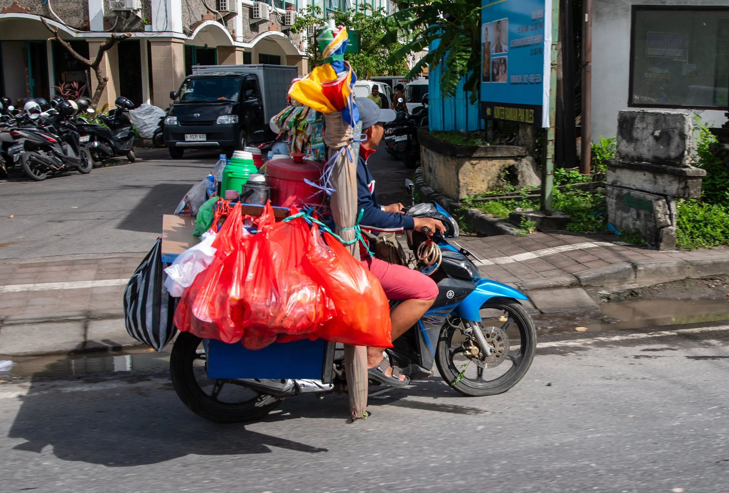 A person riding a motorcycle loaded with colorful bags and containers on a city street.