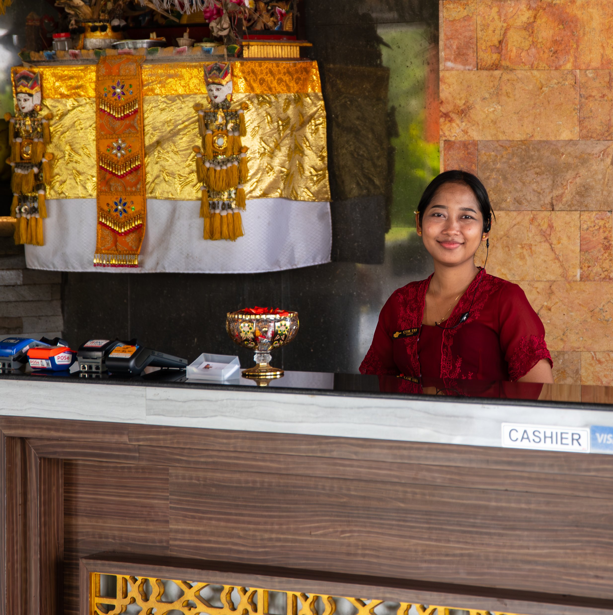 Counter with Halloween decorations, including a skeleton figure, candles, and a gold tablecloth. A woman in red clothing is smiling at the camera in front of the counter.