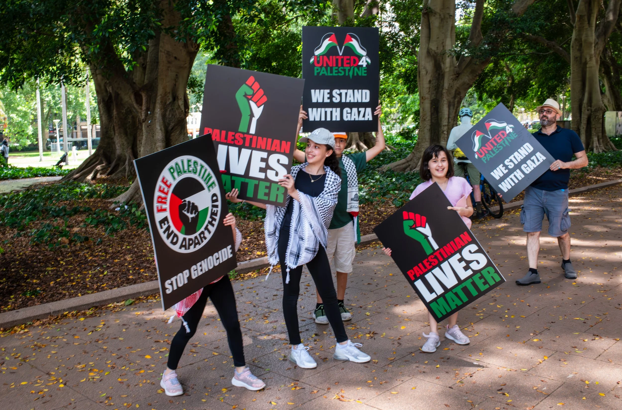 Group of people protesting with signs supporting Palestine and Gaza in a park with trees.