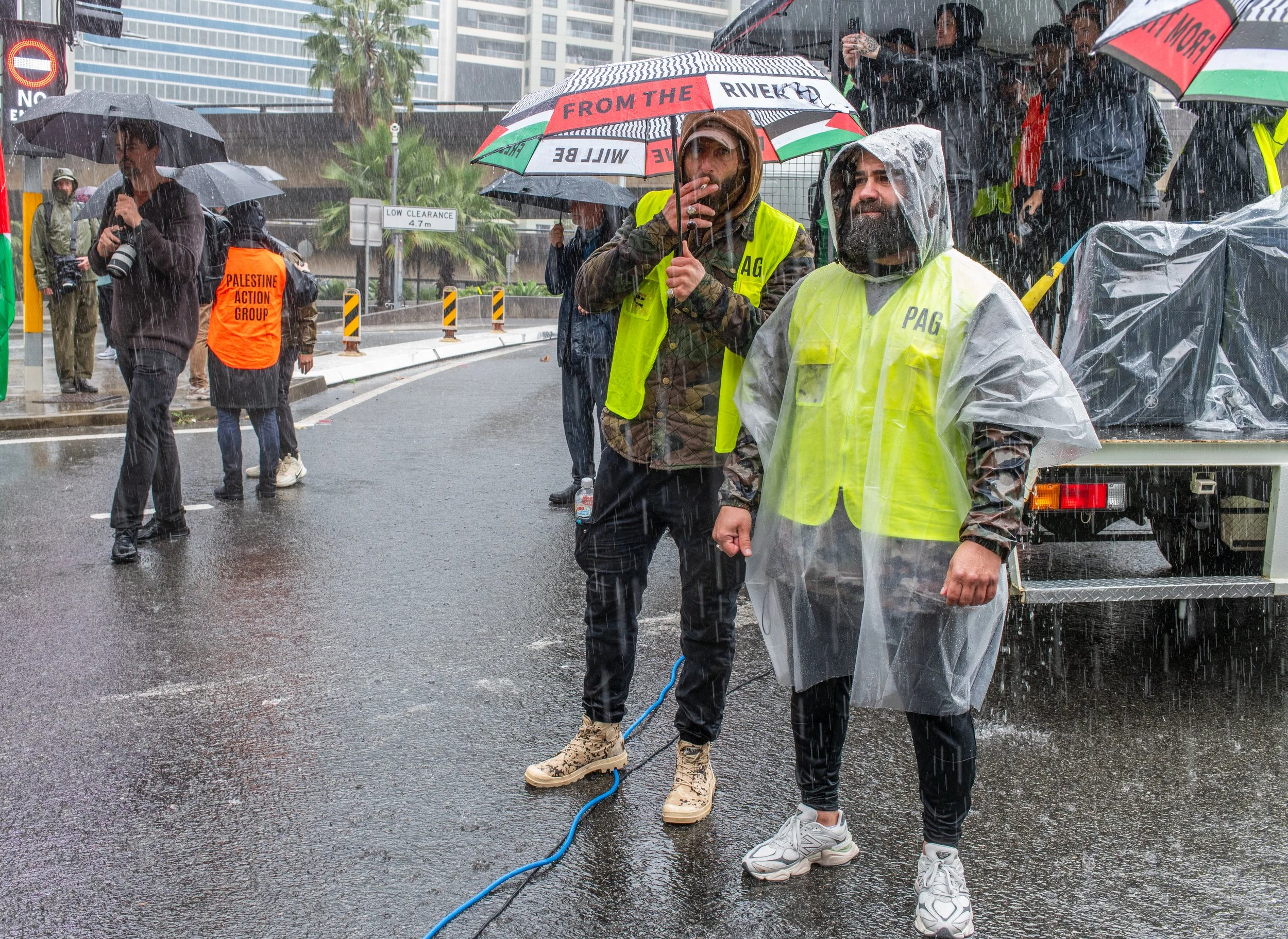 People standing in the rain with umbrellas and rain ponchos during a protest or event on a city street.