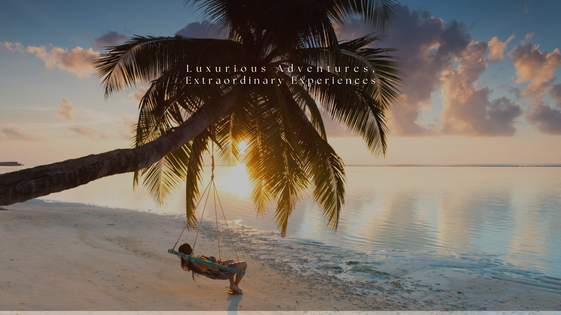 A woman relaxing on a swing hanging from a palm tree on a beach during sunset, with calm water and partly cloudy sky in the background.