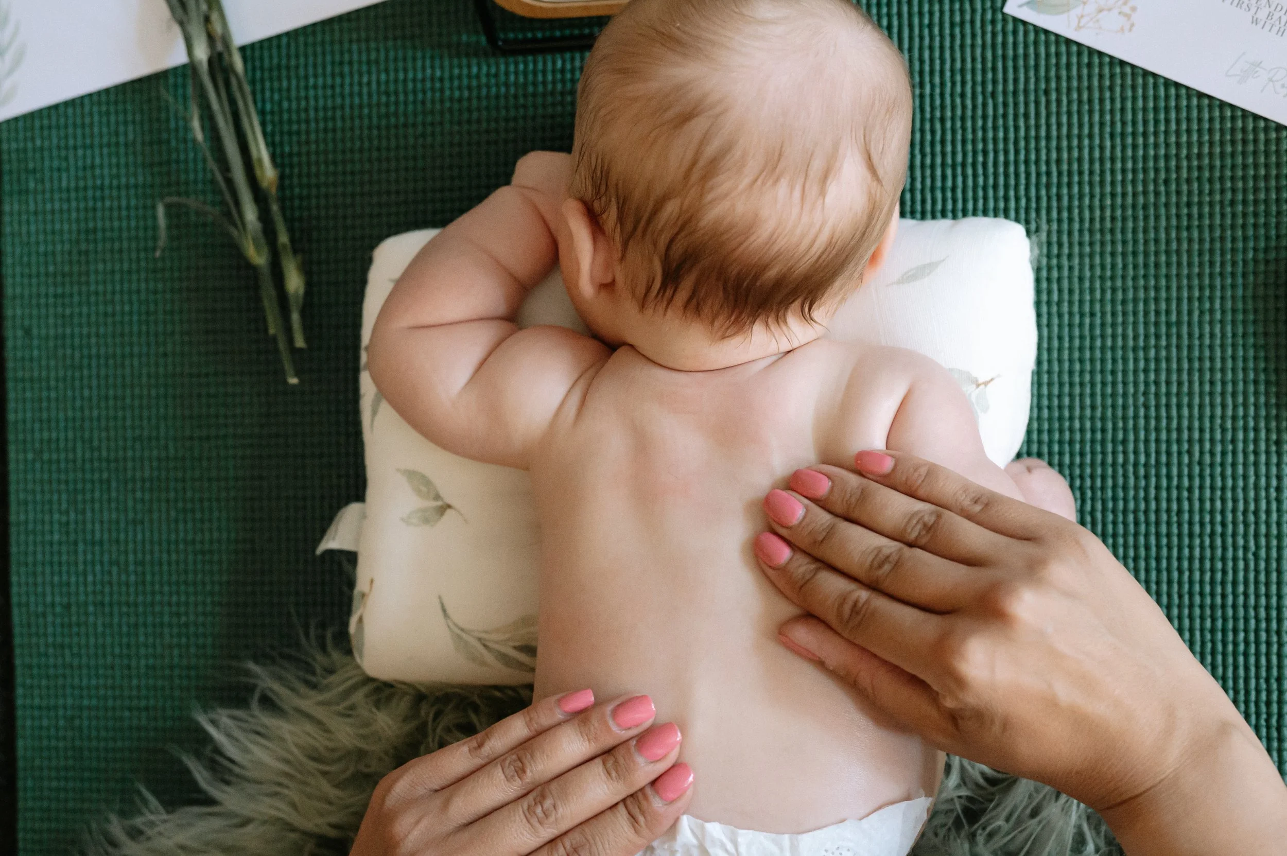 Beautiful baby massage photo. A baby having a back massage on a green mat and comfy rug, by their caregiver