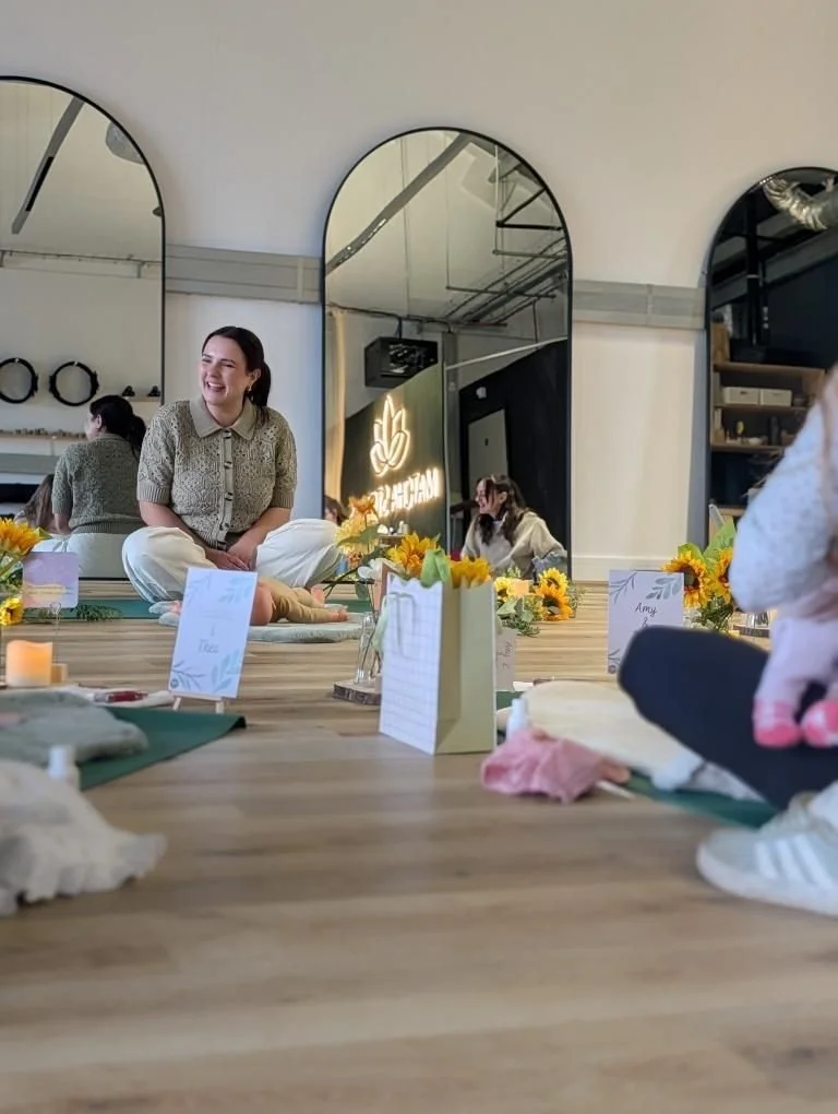 Young woman sitting cross-legged on the floor in a room with mirrors, flowers, and name cards, smiling and enjoying a social event.
