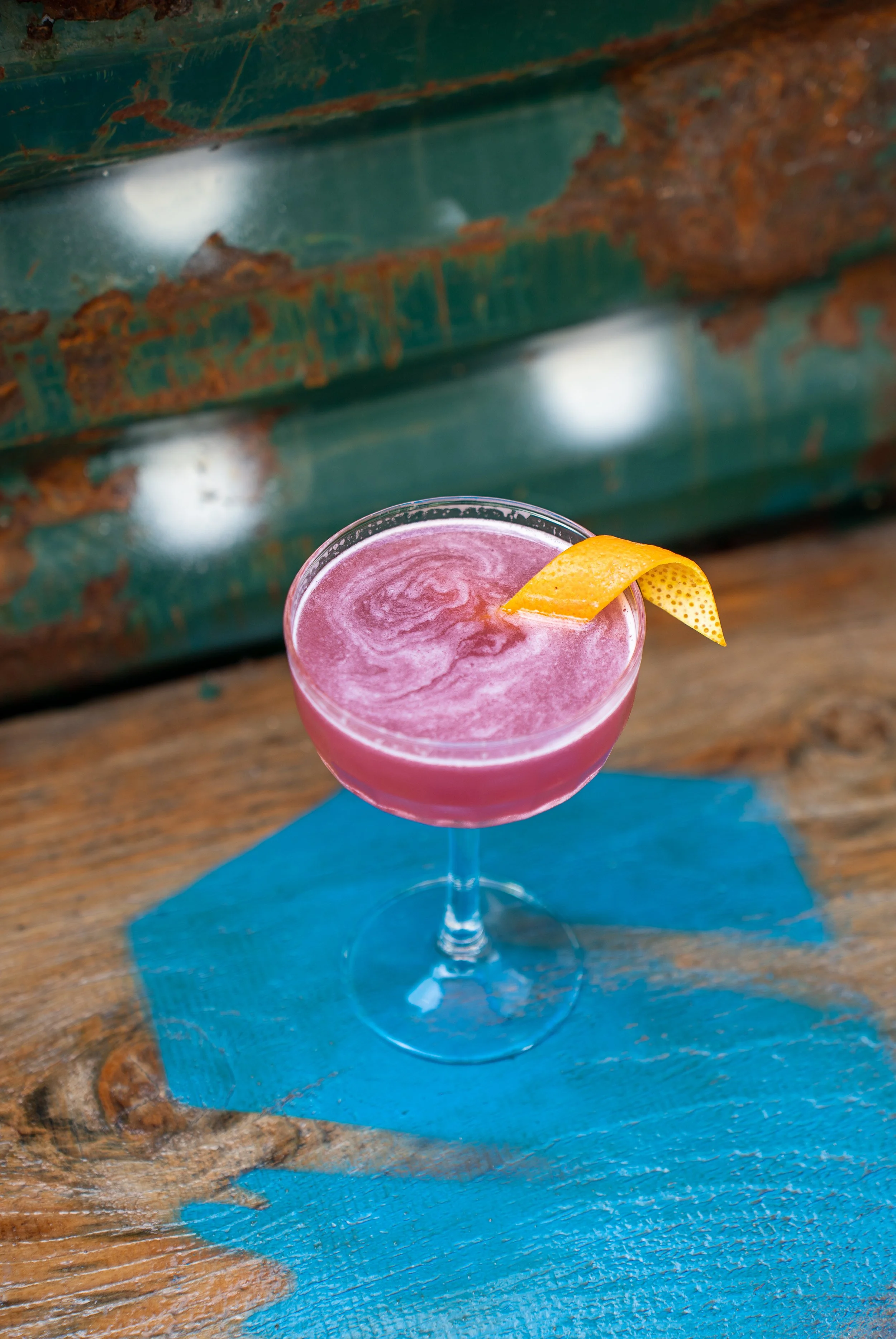 Cocktail rose avec une tranche de citron en décoration, placé sur une serviette bleue, sur une surface en bois rustique.