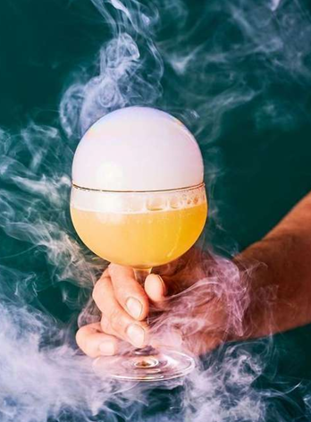 Verre de cocktail fumant tenu par une main, avec de la vapeur autour.