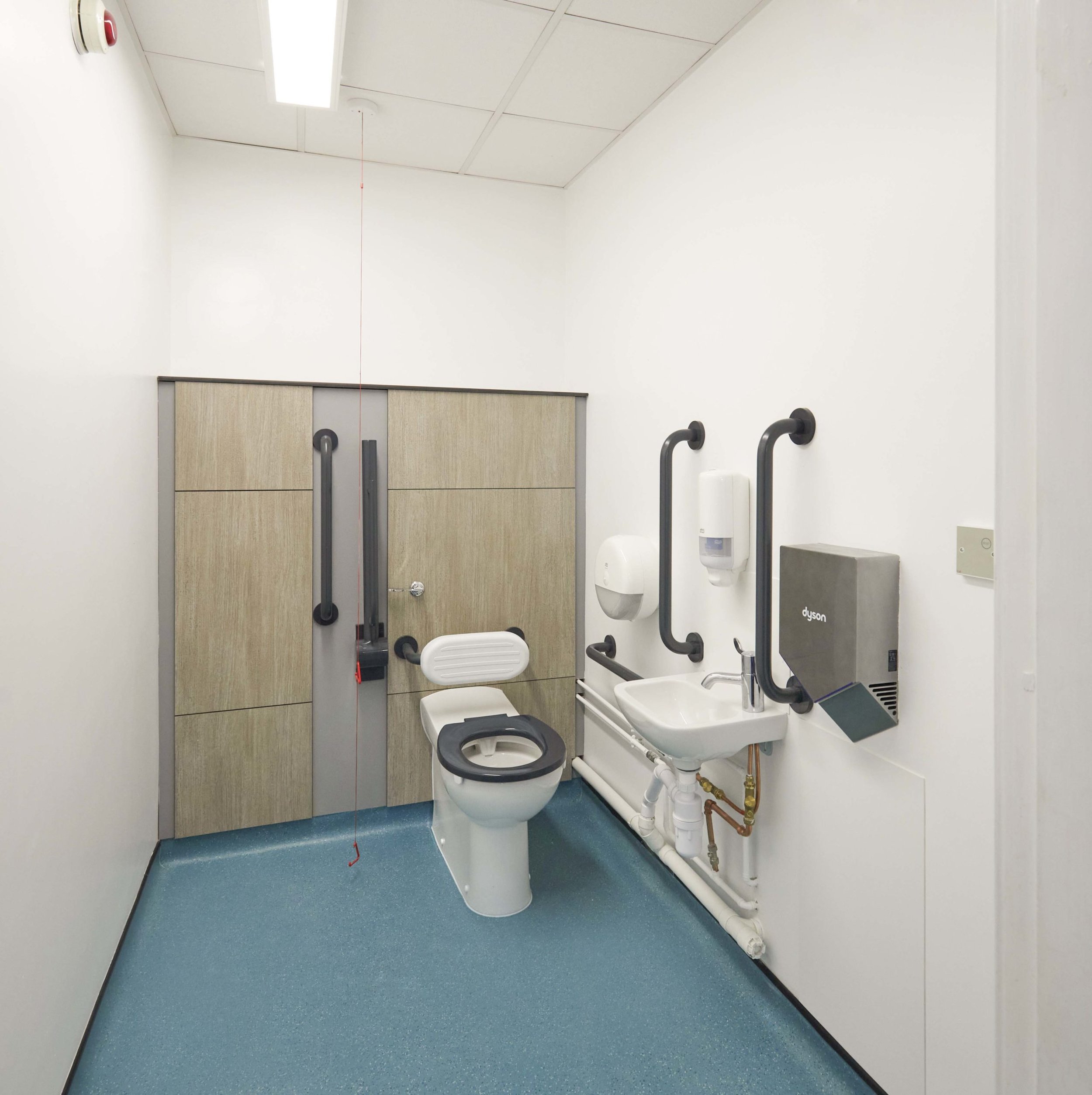 disabled doc m toilet with grey woodgrain ducts a sink, a blue floor and a dyson hand dryer at upland school.jpg
