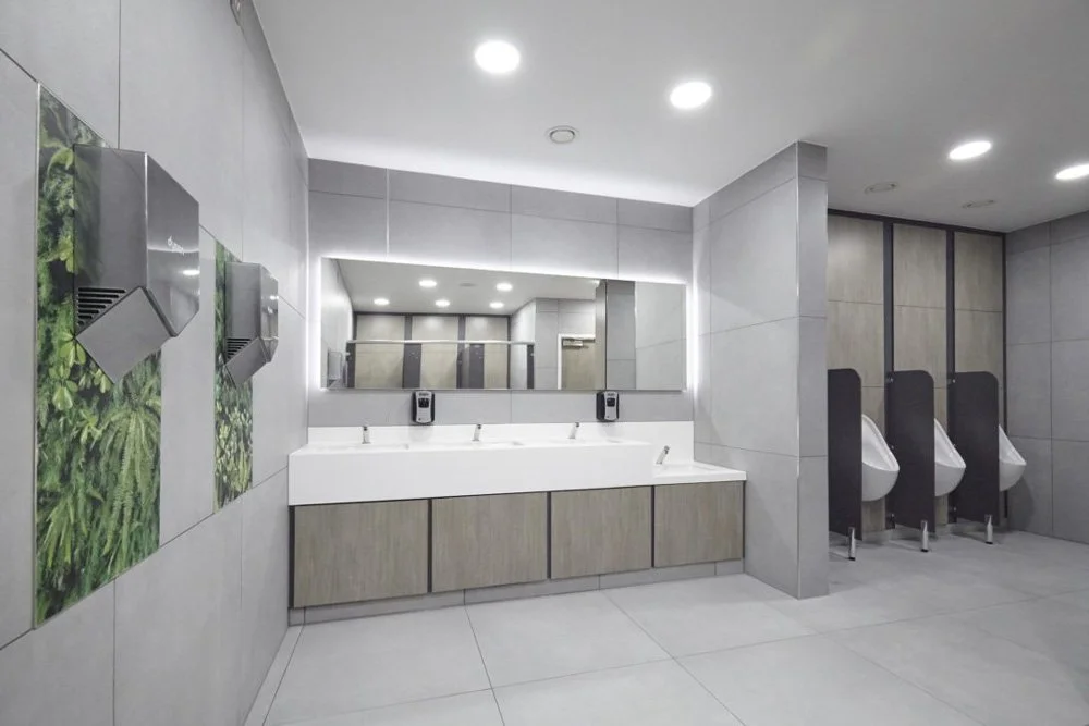 Modern public restroom with two sinks, a large mirror with integrated lighting, and three urinals, all with clean, minimalist design.