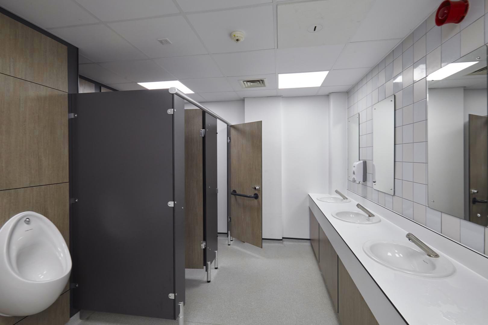 male washroom at leicester college with woodgrain urinal ducts, cubicles and a vanity unit hand wash area with feature tiling and mirror at leicester college.jpg