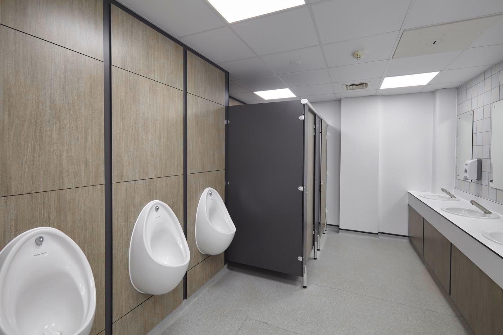 male washroom at leicester college with urinals, cubicles and a vanity unit hand wash area in woodgrain and grey at leicester college.jpg