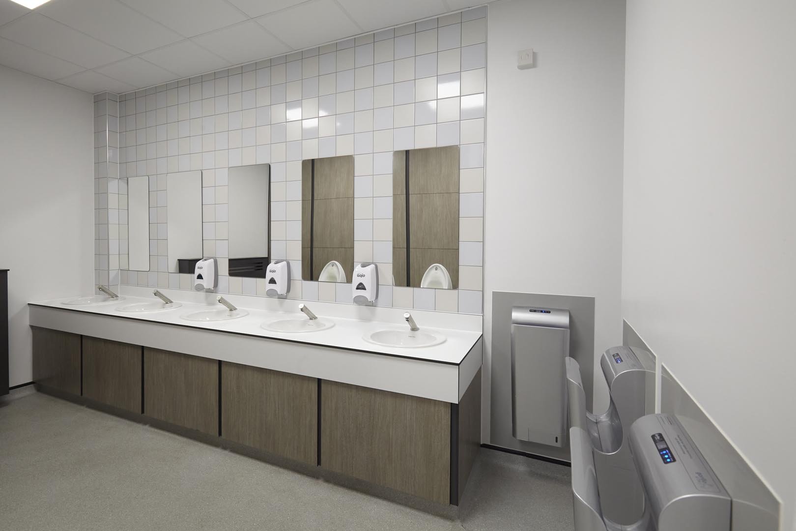hand wash area with feature white tiling, a vanity unit in woodgrain with sinks and mirrors above, high-speed dryers at leicester college.jpg