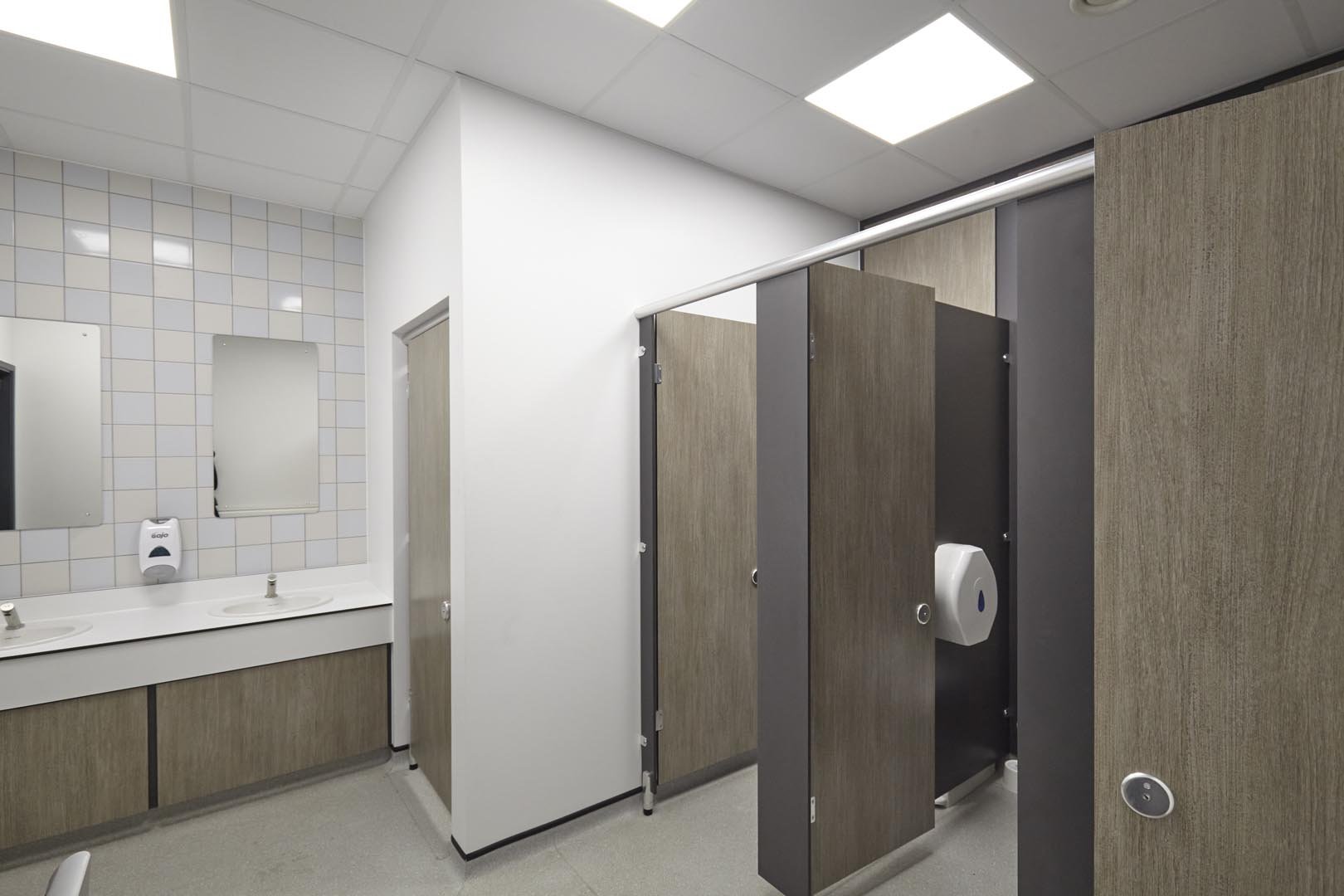 male washroom at leicester college with woodgrain toilet, cubicles and a vanity unit hand wash area with feature tiling and mirror at leicester college.jpg