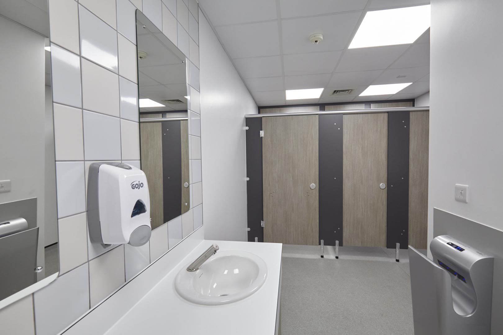 male washroom at leicester college with woodgrain toilets cubicles and a vanity unit hand wash area with feature tiling and mirror at leicester college.jpg