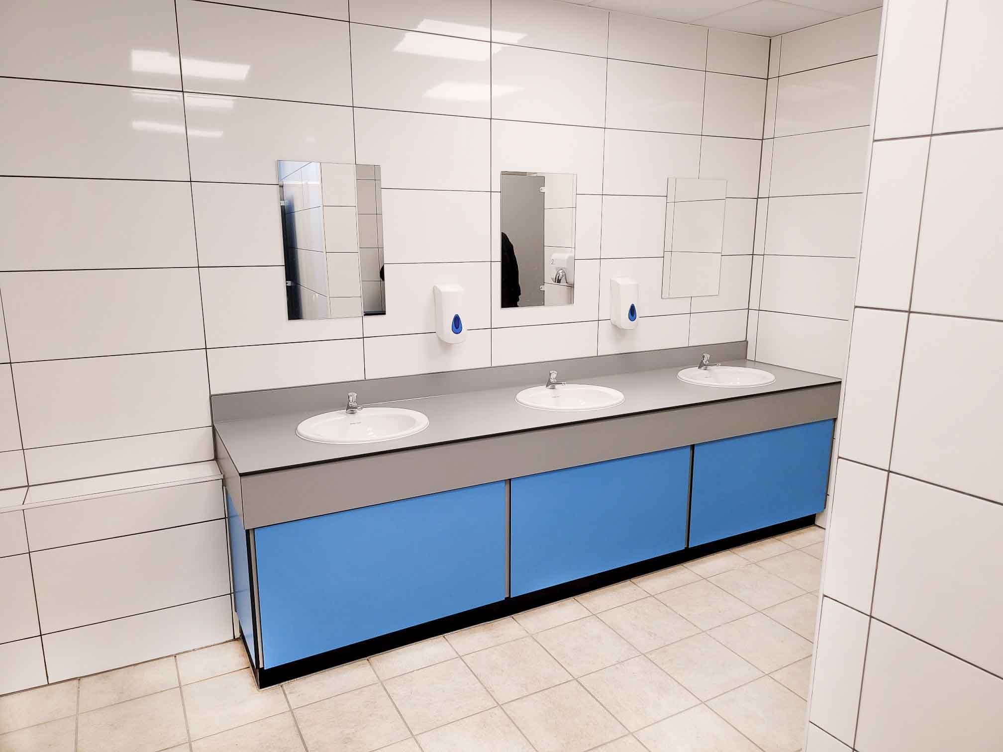 a tiled hand wash area with a blue and grey vanity unit with sinks and mirrors at herons leisure centre.jpg