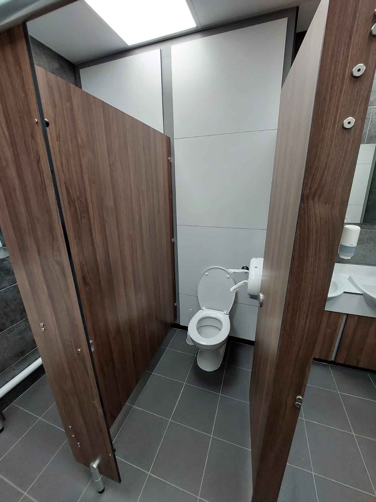 toilet cubicle with dark brown woodgrain cubicles, white full heigh duct panels and grey concrete tiling at kia oval.jpg