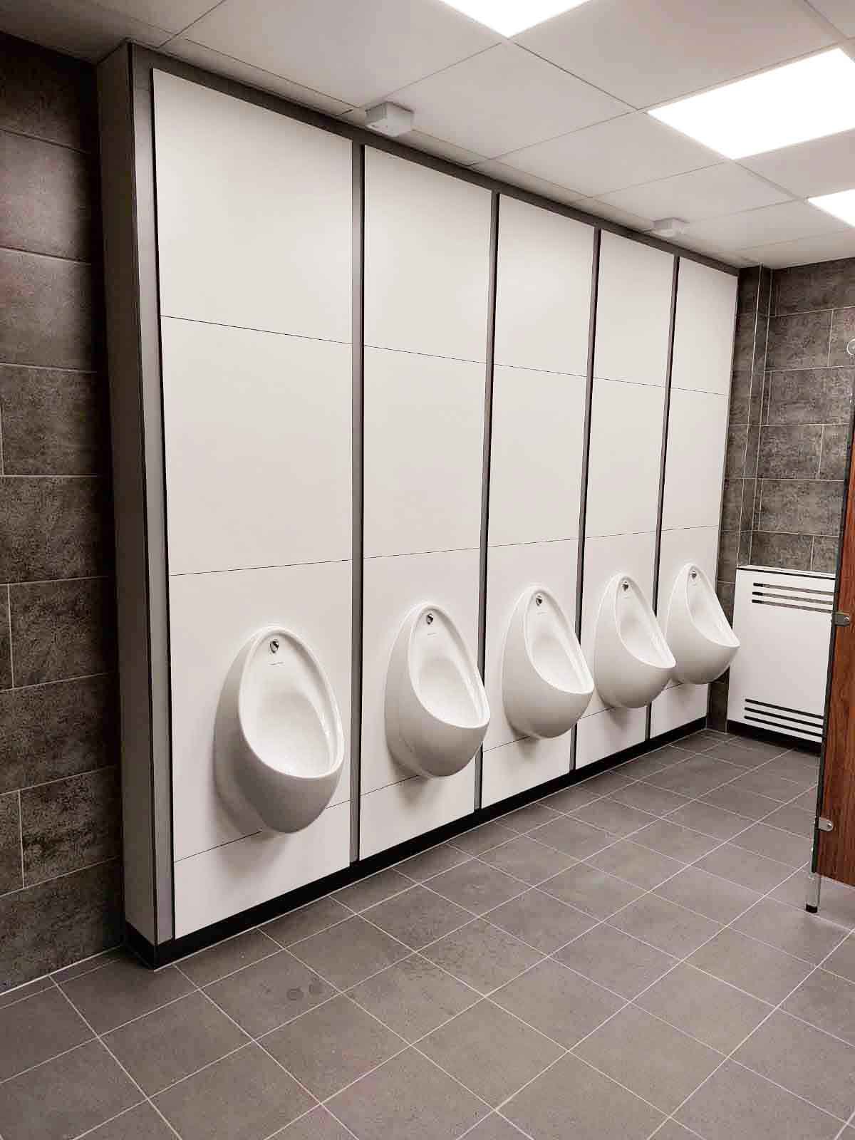 a washroom with grey tiling and a row of white full height duct panels with urinals.jpg