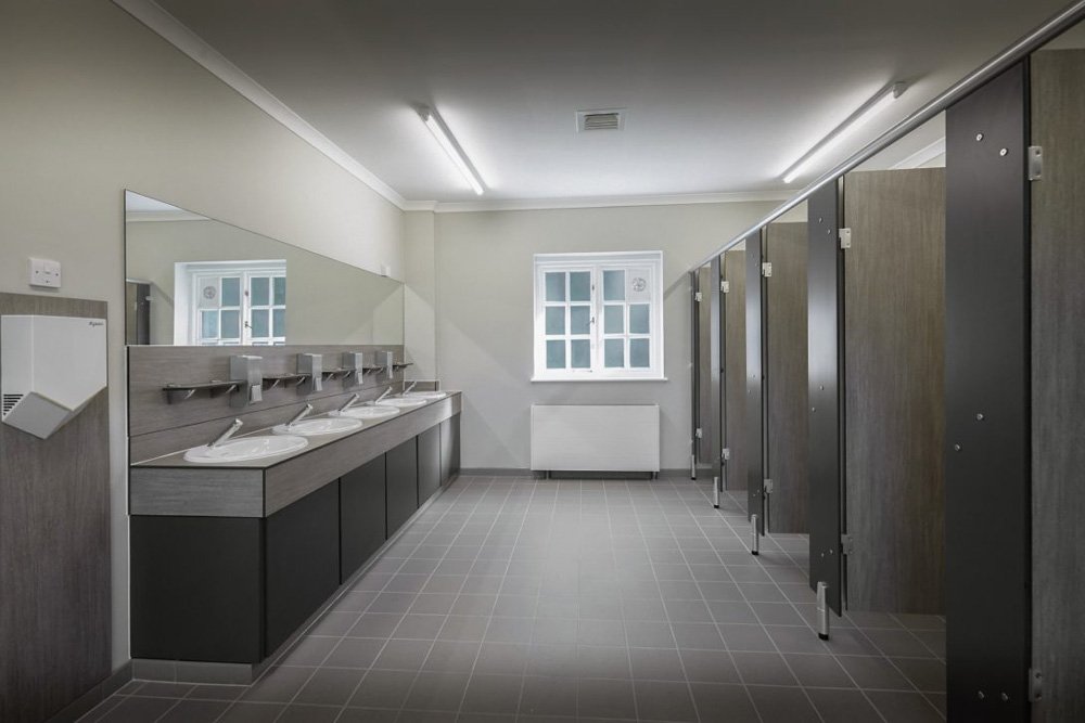 waterclose meadows campsite washroom block with grey woodgrain cubicles, a vanity unit with sinks and a splashback with shelves and dispensers and a mirror.jpg