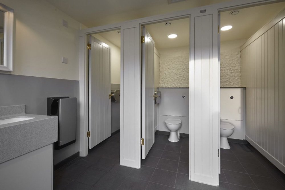 toilet cubicles with half height ducting, grey half height wall cladding and tiled floor at hughenden manor.jpg