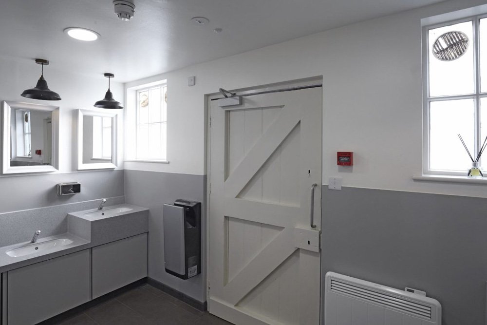 washroom with vanity unit with corian tops and a lower station with industrial lighting above and an entrance door at hughenden manor.jpg