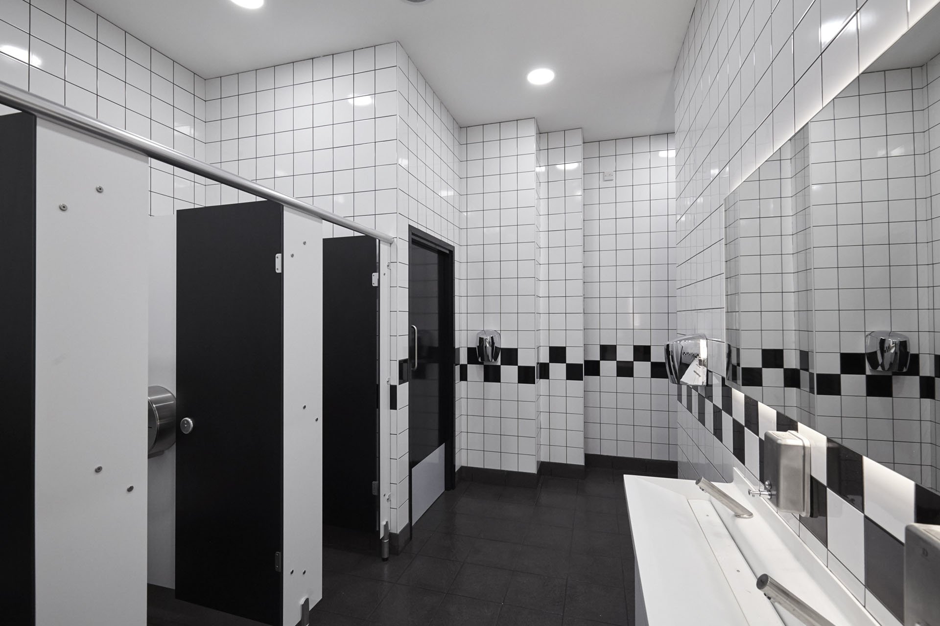 washroom at coventry bus station with black & white metro tiles and toilet cubicles, white vanity unit with solid surface trough & soft touch taps and backlit mirror.jpg