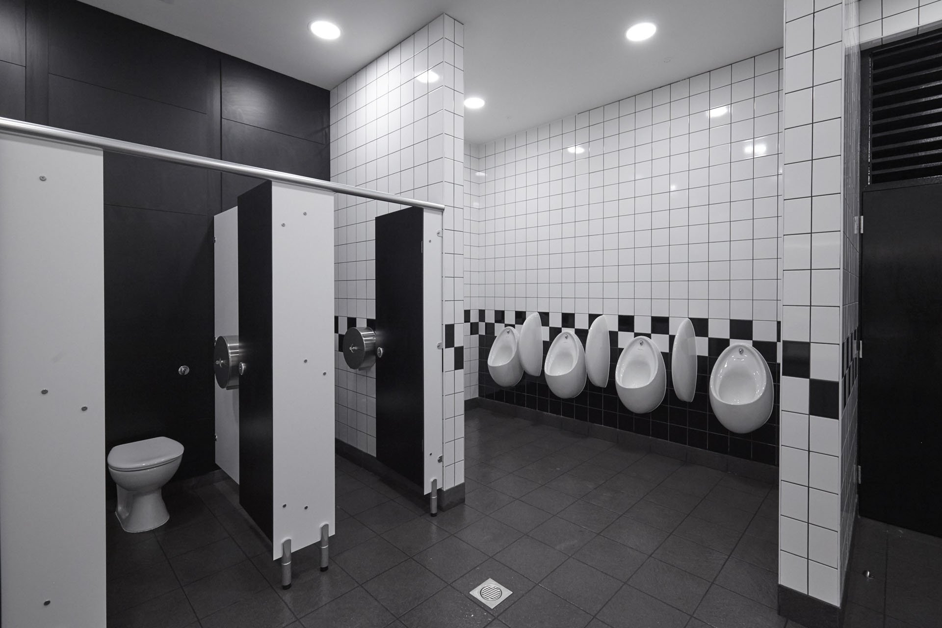 coventry bus station washroom with grey full height duct panels, black and white toilet cubicles, black and white tiling and urinals.jpg