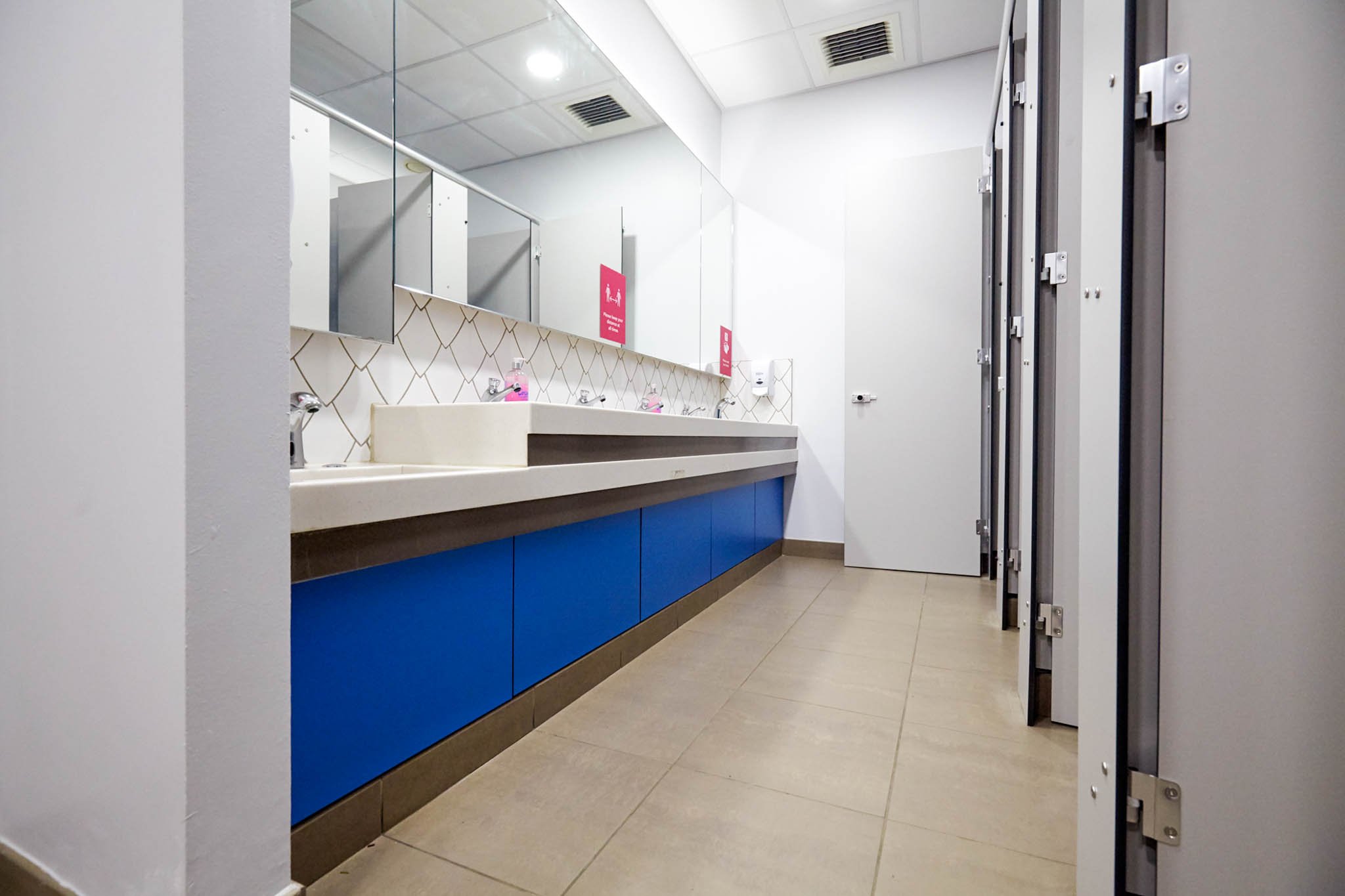 washroom with grey cubicles and blue vanity hand wash area with hand wash trough and mirrors above at national maritime museum.jpg