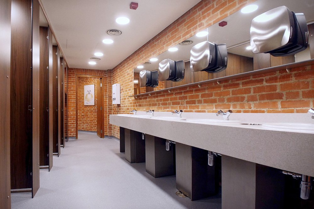 woodgrain toilet cubicles and vanity top with sinks, mirrors and silver dispensers.jpg