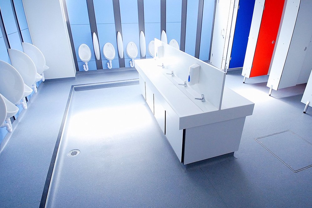 washroom with urinals and blue duct panels around the edge of the room, a hand wash station in the centre and tricolour cubicles at lycee francais.jpg