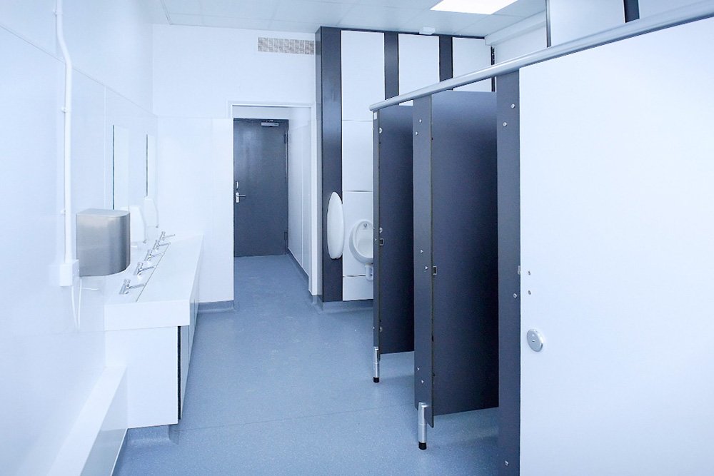 male washroom with urinals, grey cubicles and vanity unit with solid surface trough and soft touch taps at lycee francais.jpg