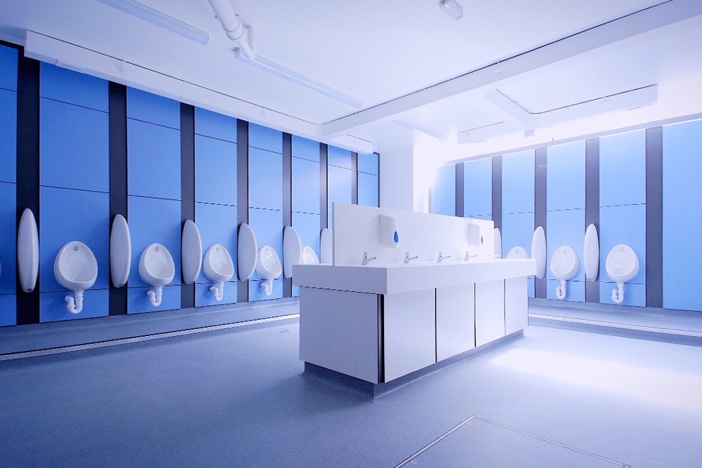 large washroom with blue duct panels and urinals on two walls and a vanity hand wash station in the centre at lycee francais.jpg