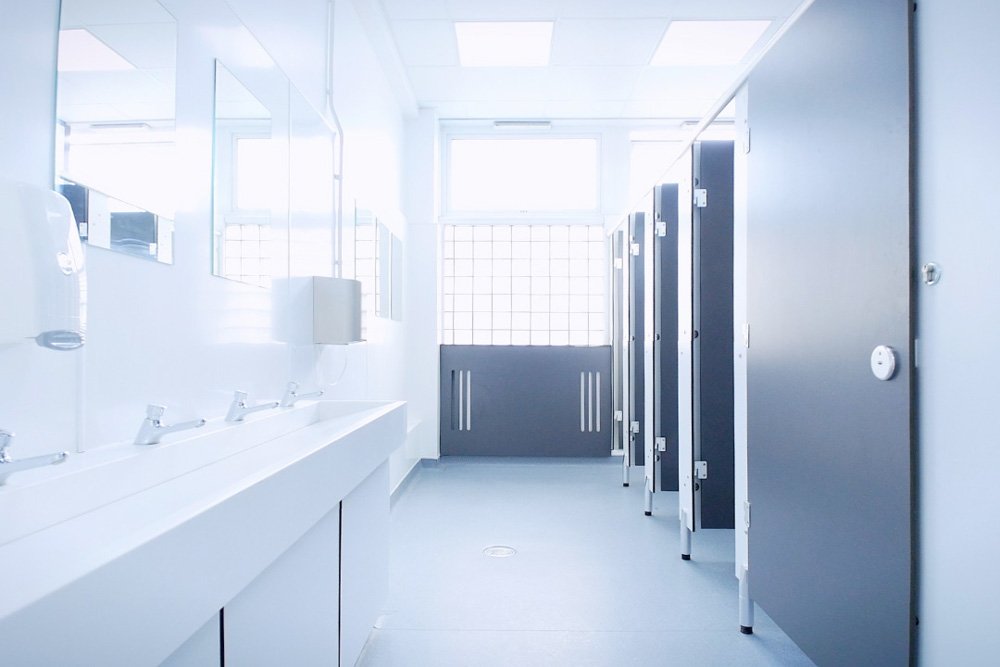 Neutral washroom with a row of cubicles, a discabled cubicle, a radiator cover and a vanity unit with a solid surface trough and soft touch taps at lycee francais.jpg