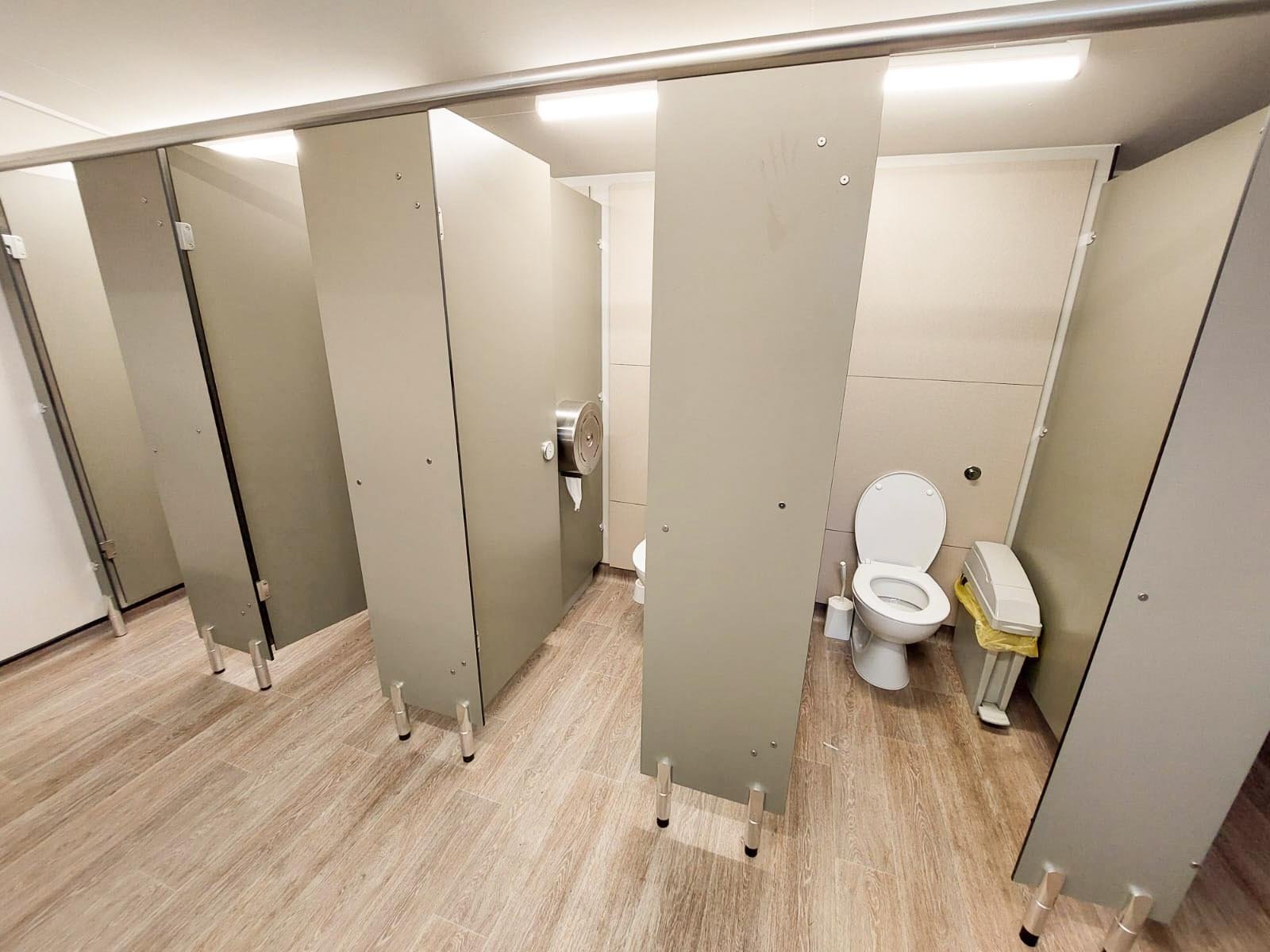 row of toilet cubicles with full height duct panels in a bespoke green colour with a woodgrain vinyl floor at howletts zoo.jpg