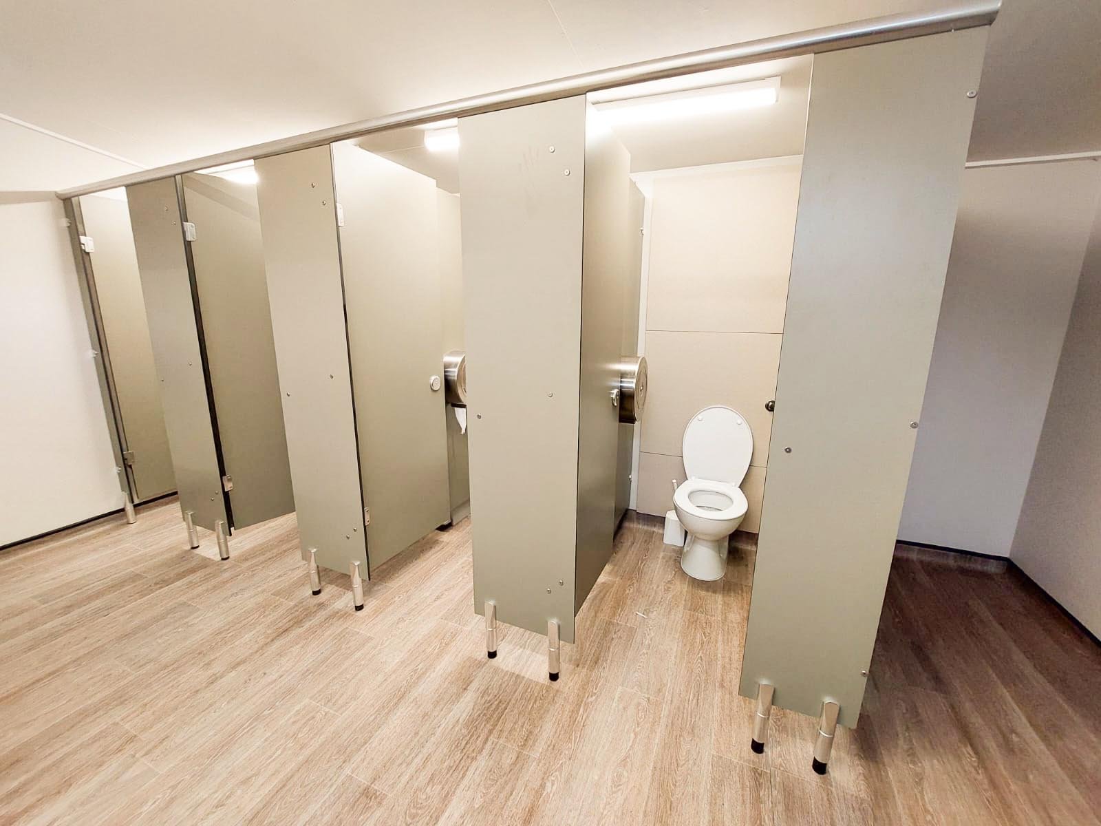 a row of toilet cubicles with full height duct panels in a bespoke green colour with a woodgrain vinyl floor at howletts zoo.jpg