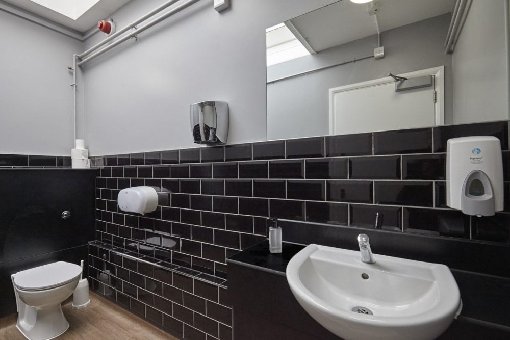 tiled black and white staff washroom with a toilet and a sink vanity unit with a mirror above at Harris Academy Philip Lane.jpg