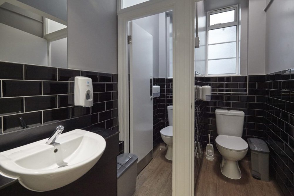 tiled black and white staff washroom with cubicles and a sink vanity unit at Harris Academy Philip Lane.jpg