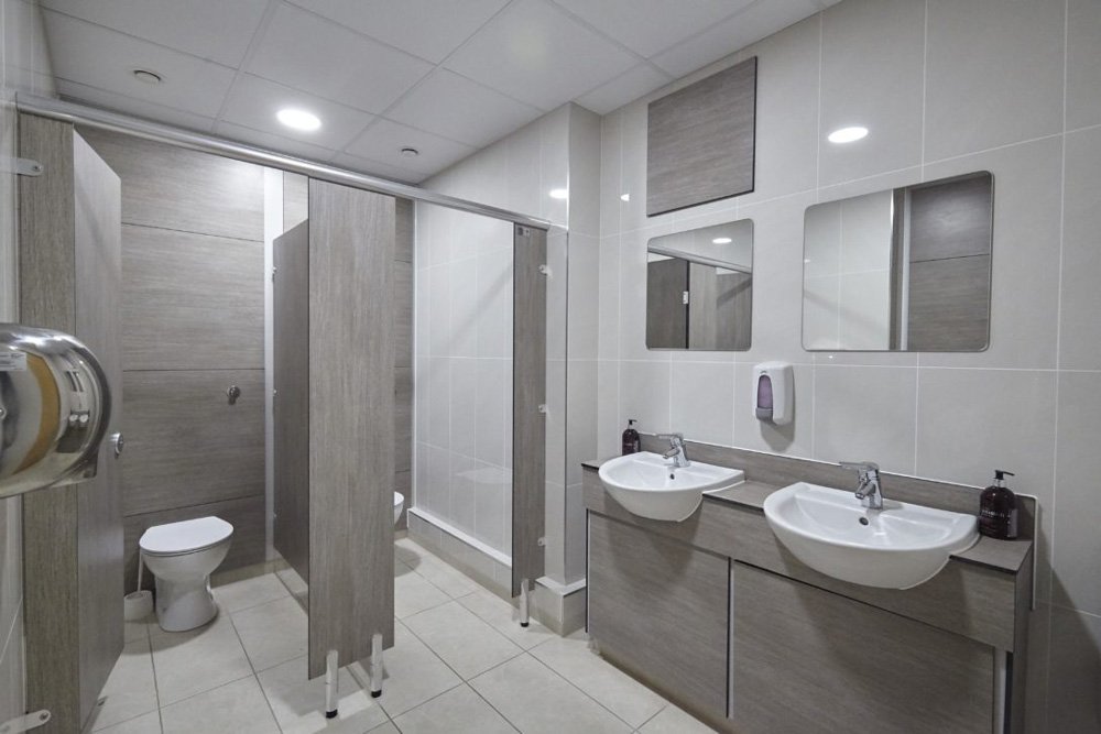 cream tiled washroom with woodgrain full height ducts, cubicles and vanity unit with sinks and mirrors above at lenta business centre.jpg