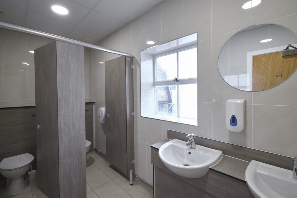 cream tiled washroom with woodgrain half height ducts, cubicles and vanity unit with sinks and mirrors above at lenta business centre.jpg